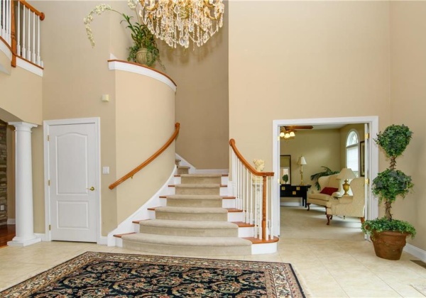 Foyer with chandelier, curved staircase and doors to den