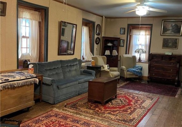 Living room with hardwood floors, many windows and two ceiling fans.